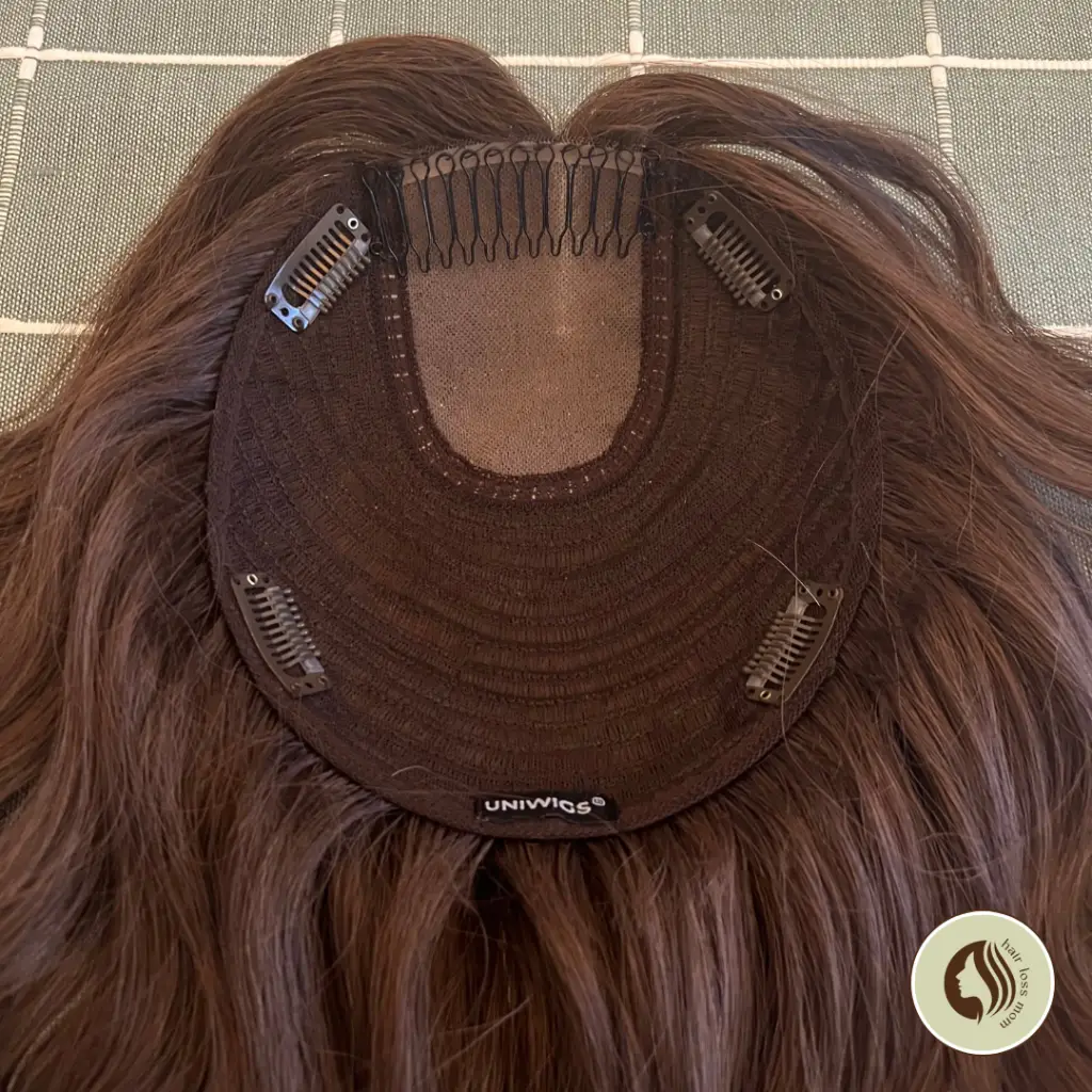 The inside of a uniwigs Courtney hair topper, showing 4 clips and a comb.