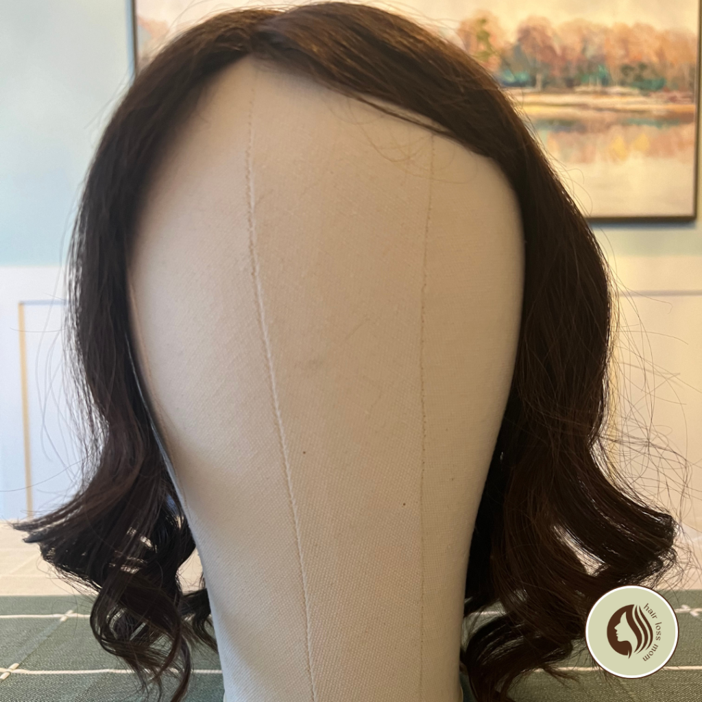 Courtney mono upgrade topper from uniwigs in truffle brown. It's on a canvas mannequin head in the centre of a dining room table, styled with curls.